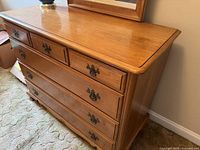 Solid wood dresser with medium-tone finish, five drawers visible from front angle.