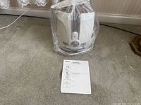 White Homedics ultrasonic cool mist humidifier in plastic wrap with visible control knob and label, placed on carpet. Manual guide sheet in front.