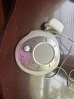 HoMedics SoundSpa sound machine placed on a wooden surface with original white power adapter attached by a cord.