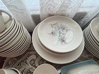 Stack of creamy white porcelain plates with pink and blue floral pattern, showing salad plates and dinner plates with teacups on top.