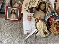 Close view of religious paper items including calendar with Jesus image, Pope Francis photo, prayer cards, and a Virgin Mary bust