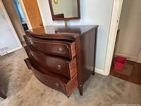 Side view of the mahogany dresser showing three bowed drawers and brass pulls, with visible surface wear on top.