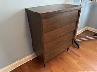 Front side view of mid-century modern 4-drawer dresser, showing woodgrain laminate finish and tapered legs.