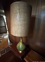 Full view of the tall table lamp showing green drip glaze ceramic base and tall burlap-wrapped drum shade.