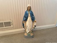 Full-body statue of Virgin Mary in blue cloak and white robe, standing on hexagonal base