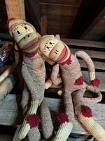 Two vintage handmade sock monkeys posed leaning together, showing full front view, facial features, and red pom-pom details