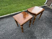 Pair of two vintage wood accent tables shown outside on pavement, square and demi-lune shape, showing woodgrain finish and spindle legs.