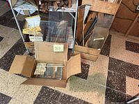 Photo showing cardboard box with precut metal pieces, scrap wooden pieces nearby, and part of two textured metal carts on wheels.