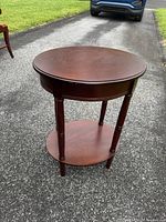 Front angled view of the round cherry wood accent table showing top surface, legs and lower shelf.