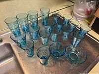 Full set of blue bubble-pattern glassware arranged on a countertop near sink, shows various tall and small glasses, and a bowl with textured bubble design.