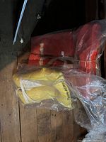 Red adult life jacket and yellow child life jacket in plastic packaging on wooden floor.