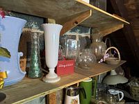 First image shows upper attic shelf with multiple decorative vases, goblet, ceramic mug, hand-painted chicken figurine, swan dish, and other decor items arranged across the shelf.