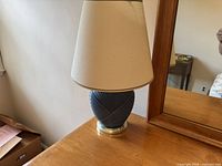 Photo of a small table lamp with cream lampshade and green ribbed base featuring brass detailing on a wood surface