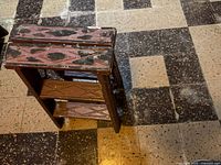 Side and angled view showing the step stool with purple paint, diamond pattern details, and visible wear on wooden floor tiles.