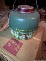 Photo of vintage Bonnie Jug metal beverage dispenser showing green upper body, retro plaid pattern on lower part, red screw-on lid, metal handle, and spout on front.