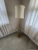 Full view of the vintage lamp with ivory drum shade in a corner near windows with lace curtains.