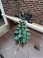 Full view of vintage green ceramic lighted Christmas tree with attached power cords on outdoor surface