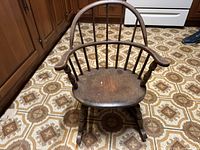 Front view of vintage wooden child’s Windsor-style rocking chair highlighting spindle back and well-worn seat.