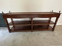 Front view of the wood console table showing three open shelves and decorative finials on top corners.