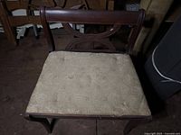 Front view of vintage wooden side chair showing upholstered seat with fabric wear and decorative X-style curved backrest.