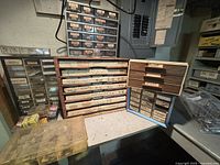 Multiple labeled drawer units containing a variety of screws, fasteners, clamps, springs, chisels, and punches in wooden and plastic drawers. Assorted hardware visible in jars and test tubes.
