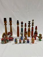 Full frontal photo showing all 19 wooden figurines arranged in 3 rows including the candlestick holders, tall girl figurines, ornaments, a horse, a bird whistle, and 5 Russian doll keychains.