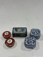 Five trinket boxes including two red and gold Leart Porcelain, two blue and white ceramic hexagonal, and angel stained glass music box