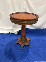 Front side view of the antique round accent table showing the wood top, carved details, and metal trim on base with paw feet.