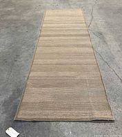 Full view of the beige, tan, and gray striped hallway rug laid flat on a concrete floor showing overall condition and shape.