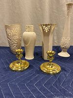 Overview photo of four Lenox white porcelain vases with gold accents and two Baldwin polished brass candle holders on blue quilted pad