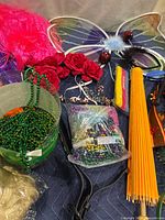Overview of costume accessories, including wig pieces, butterfly wings, fans, flower headbands, and Mardi Gras beads spread out on blue fabric.