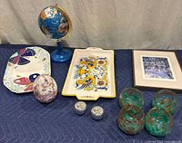 Lot with votive holders, decorative trays, framed print, globe, and decorative ceramic plate shown on quilted dark blue background
