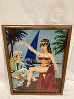 Front view of the framed needlepoint art showing the scene of Middle Eastern dancer and musician with palm trees and sailboat background.
