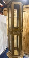 Front and side view of vintage octagonal glass display cabinet with wooden frame and carved detailing. Internal three glass shelves visible along with internal wiring for light fixture.