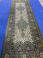 Full view of the rug showing the entire length with central medallion and border design in green, gold, beige, and black colors on blue background.