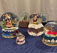Seven assorted snow globes on table showing various holiday and landmark themes