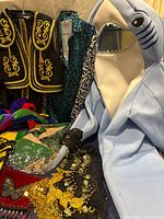 Photo of assorted adult costumes including matador jacket, teal robe, shark costume, and jester hat along with bee costume cape and other accessories.