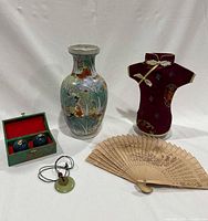 Five-piece Asian lot with porcelain vase, decorative wine bottle cover, wooden fan, Baoding balls in box, and jade pendant necklace, arranged on white background.