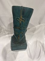 Front-left angled view of the teal and gold Nefertiti bust sculpture showing the headdress and facial features on a square base.