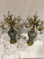 Pair of green marble and brass electric candelabra lamps with five arms each, displayed side-by-side with cords visible.
