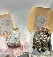 Both dolls displayed on a flat surface with original boxes in background, showing their size difference and packaging.
