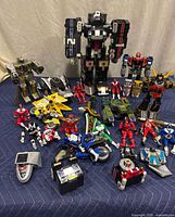 Wide view showing large Megazord toys center back with surrounding Power Rangers figures and various vehicle toys including motorcycles and tank; weapons and components arranged in front