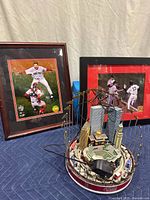 Diorama with Boston city skyline miniatures, ballpark and figurines, with two framed photos behind it and power adapter in foreground.