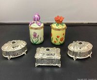 Photo of all five items: two ceramic candle holders with floral lids and three ornate metal trinket boxes arranged side by side.