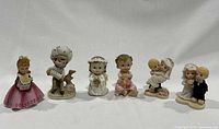 Photo showing all six figurines arranged in a row, including children, angels, and wedding couples in pastel colors and varying sizes.