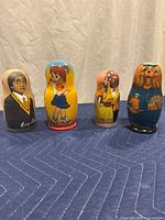 Front view of the four hand-painted wooden nesting dolls in mixed themes set on a blanket.