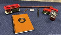 Overview of all items: whip, lighter, pocketcutter, two red cable car/bus models, letter opener, Celtics notebook, panda globe trinket