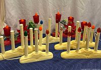 7 vintage electric Christmas candle window lights with mixed red and ivory plastic bodies, different colored flame bulbs, and cords laid out on blue fabric with backdrop.