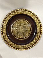 Front view showing dark brown glossy wooden plate with intricate geometric inlay pattern made of Mother of Pearl in the center and around the rim.