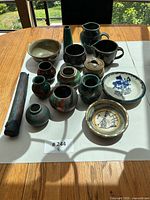 Top-down photo of 15 handcrafted pottery pieces on a table with natural light from window behind, showing various vases, pitchers, jars, plates and cylindrical piece.